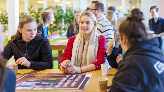 Leerlingen luisteren in een groepje aan tafel.