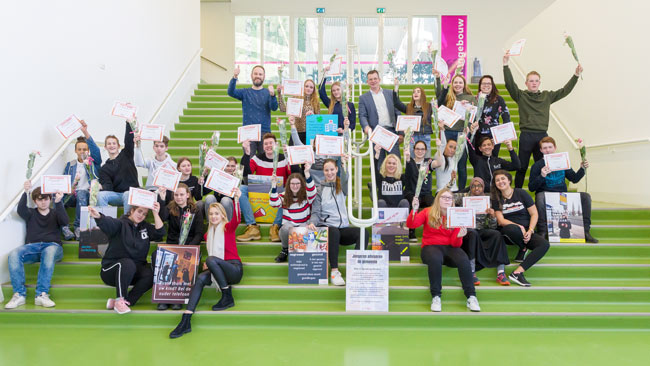 Groepsportret op een groene trap van leerlingen met hun project resultaat en behaald certificaat